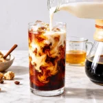 Glass of iced coffee with ice cubes and creamy swirl in a kitchen setting