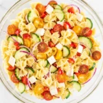 Fresh Pasta Salad with tomatoes, cucumber, mozzarella, and Italian dressing in a serving bowl