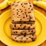 Freshly sliced Protein Banana Bread on a wooden board with ripe bananas nearby