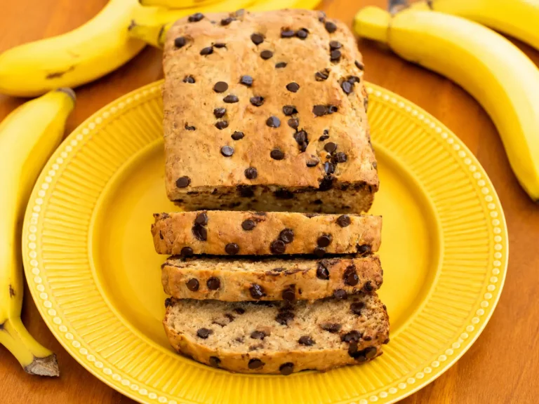 Freshly sliced Protein Banana Bread on a wooden board with ripe bananas nearby