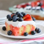 Strawberry Jello Flag Cake topped with whipped cream, strawberries, and blueberries