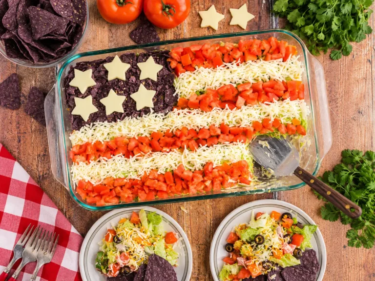 Taco Salad Flag layered dip topped with tomatoes, mozzarella, and blue tortilla chips
