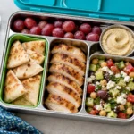 Hummus Pita Bento Box with cucumber salad, hummus, pita bread, grapes, and grilled chicken