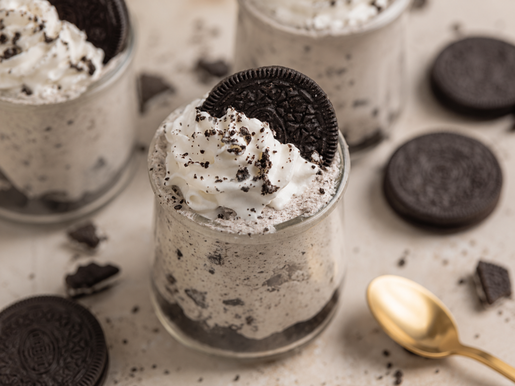 Oreo Cheesecake Cups topped with whipped cream and crushed cookies in glass dessert cups