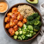 Salmon Bites Bowls with crispy salmon, rice, avocado, broccoli, cucumber salad, and bang bang sauce