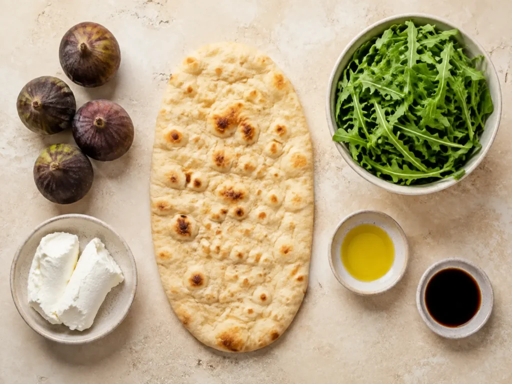 Ingredients for Fig Goat Cheese Flatbread arranged with artisan flatbread, fresh figs, goat cheese, arugula, garlic-infused olive oil, and fig balsamic vinegar